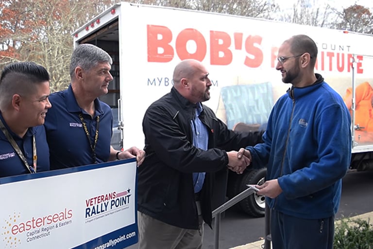 A representative from Bob's Discount Furniture presents a veteran with a gift card.